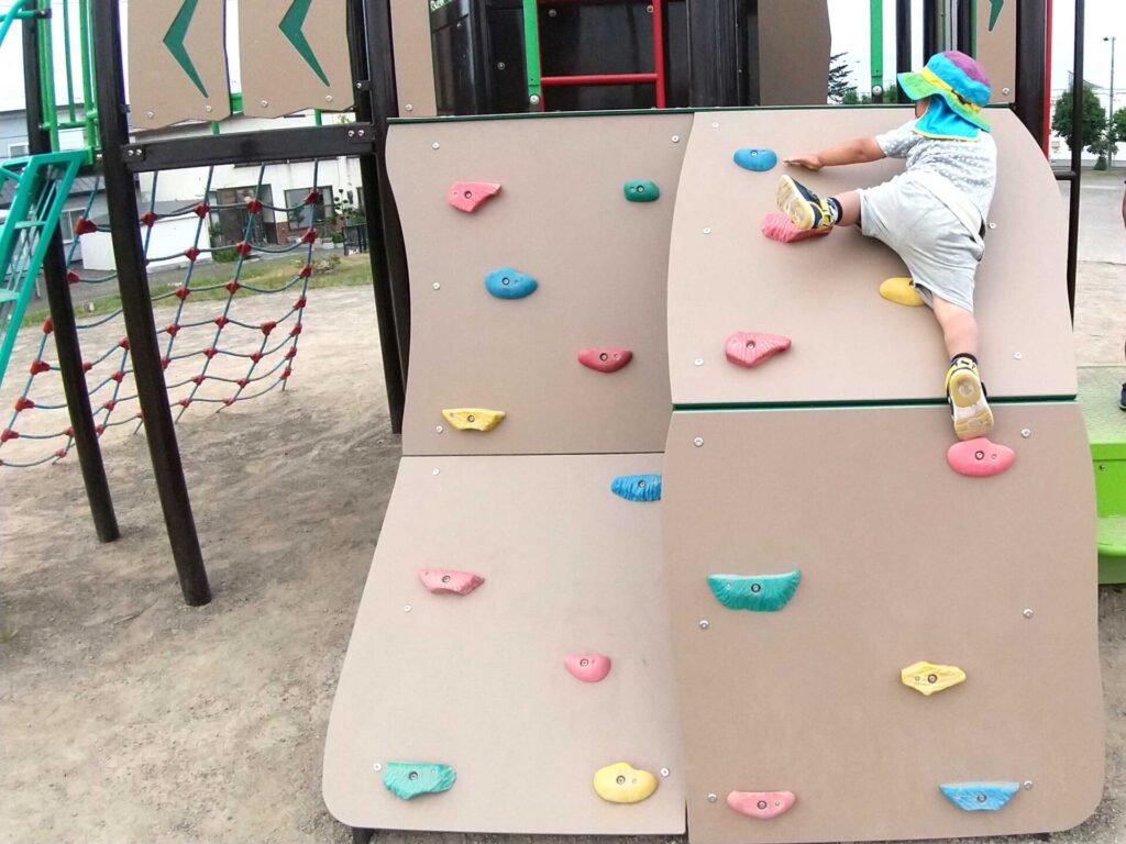 東光ふれあい公園　東側遊具　幼児が１人で登っているボルダリングの写真